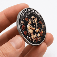 A hand holding a round commemorative coin with a detailed Day of the Dead design featuring a skeleton, skulls, and red roses on a black background, with the text 'MEMENTO MORI' around the top edge.