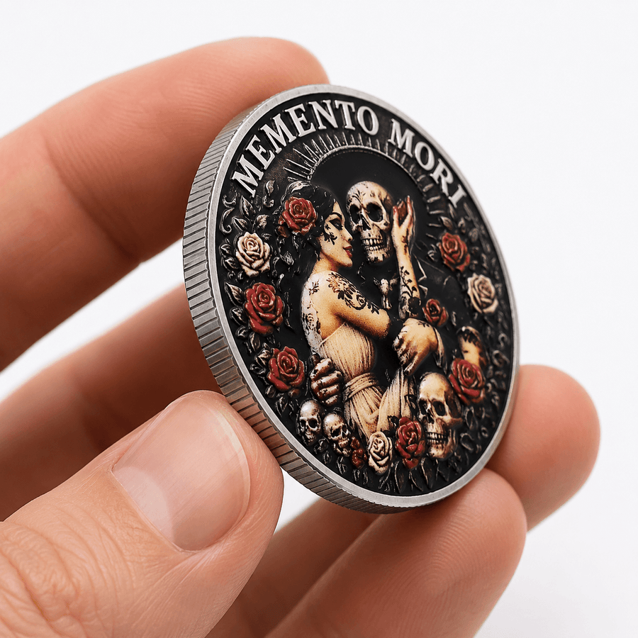 A hand holding a round commemorative coin with a detailed Day of the Dead design featuring a skeleton, skulls, and red roses on a black background, with the text 'MEMENTO MORI' around the top edge.