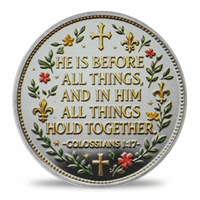 A round silver-toned religious medallion featuring the Bible verse Colossians 1:17, 'HE IS BEFORE ALL THINGS, AND IN HIM ALL THINGS HOLD TOGETHER,' with gold lettering, green leafy branches, and red floral accents.