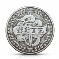 Love hate double-sided coin hate side featuring two crossed daggers or swords with HATE text on banner, serpent or snake coiled around, radiating sunburst lines in background, skulls border around outer rim, antique silver finish, 40mm diameter



