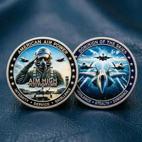 Two military challenge coins featuring fighter jets and pilots, displayed on a dark blue textured surface. One coin shows a saluting pilot with the text 'AMERICAN AIR POWER AIM HIGH FLY FIGHT WIN' and 'INTEGRITY SERVICE EXCELLENCE'.