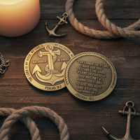 Two round brass-toned anchor challenge coins with engraved scripture and anchor motifs, displayed on a dark wooden surface with rope, candles, and small anchor charms around them.