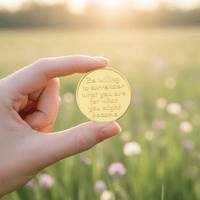 Hand holding be willing to surrender what you are for what you might become coin polished gold handwritten script spring meadow golden light transformation collectible token
