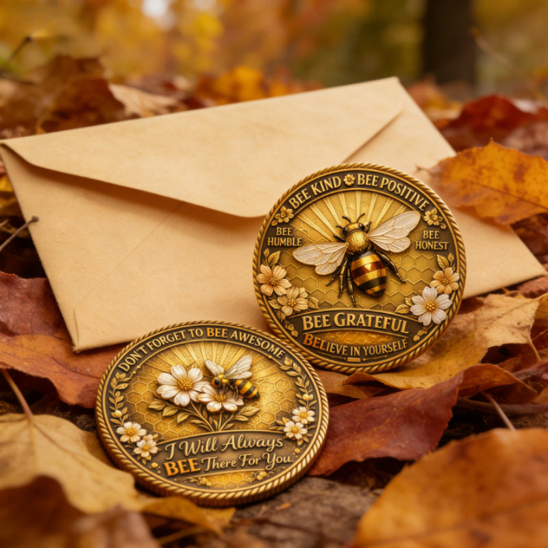 Two gold coins with bee designs on a bed of autumn leaves and an envelope.