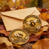 Two gold coins with bee designs on a bed of autumn leaves and an envelope.