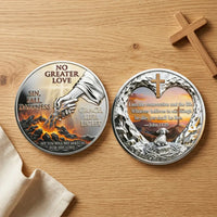 Overhead view of both No Greater Love Christian coin faces on an oak tabletop, with cream linen at the lower left and a wooden cross at the upper right. The left shows a robed arm rescuing a hand from fiery ground beneath “NO GREATER LOVE.” The right features John 11:25 within a heart-shaped rocky frame, with a cross, sunset, lamb and crown of thorns, collectible token