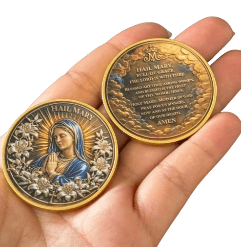 Two religious coins featuring Hail Mary, one showing a relief portrait of Mary and the other displaying the inscription, held in a person's hand against a black background.