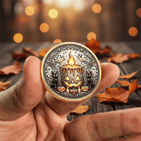 A hand holds a round gold-toned coin featuring a Halloween design with a jack-o'-lantern candle, ghosts, black cats, and pumpkins, set against a blurred background of autumn leaves and warm lights.