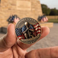 A close-up of a hand holding a round commemorative veteran coin in front of a blurred outdoor monument with American flags.