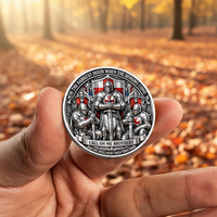 A hand holds a round silver-toned commemorative coin featuring a medieval knight and two smaller figures with red cross motifs, against a blurred autumn forest background with fallen leaves.