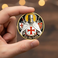 A hand holding a round commemorative coin featuring a medieval knight in armor with a white cape and red cross motif, with the words 'For the Faith' along the bottom, against a blurred warm background.