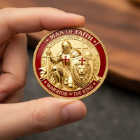 A close-up of a hand holding a round gold and red challenge coin featuring a knight with a cross, a lion shield, and the text 'MAN OF FAITH' and 'WARRIOR OF THE KING'.