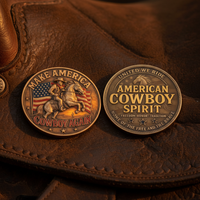 Two circular bronze-toned cowboy-themed medallions displayed on a brown leather surface. One side shows a rider on a horse with an American flag and the text 'MAKE AMERICA COWBOY AGAIN'; the other side reads 'AMERICAN COWBOY SPIRIT' with additional western text around the edge.