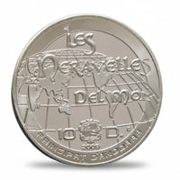 Silver coin with 'Les Merveilles Del mon' text and a globe design on a white background
