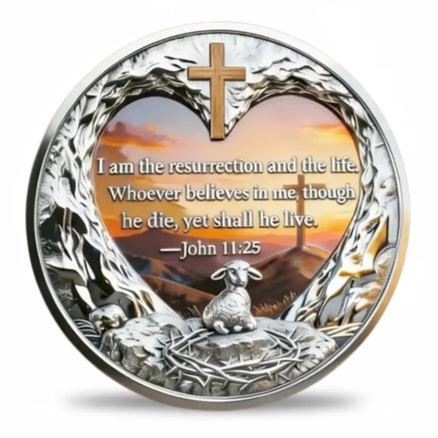 Christian coin reverse with a John 11:25 quotation inside a heart-shaped rocky frame, topped by a gold-tone cross. A sunset landscape and distant cross appear behind the verse, with a lamb and crown of thorns in the foreground, collectible token
