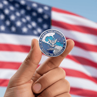 A hand holds a round commemorative coin in front of a blurred American flag. The coin is silver-toned with blue, white, and red details and reads 'BARKIN VARCOTERON' and 'RESTORE THE DEMOCRACY.