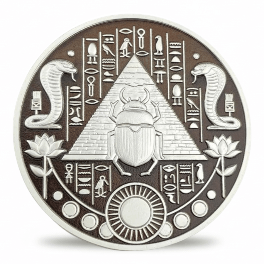 A circular Egyptian-themed coin featuring a raised scarab beetle in front of a pyramid, flanked by two coiled snakes, lotus flowers, and hieroglyphic symbols on a dark brown background with a silver-toned rim.