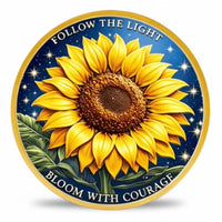 Sunflower coin with a gold-tone border, showing a fully opened yellow flower with a brown centre and green leaves against a star-filled blue background. White lettering reads “FOLLOW THE LIGHT” above and “BLOOM WITH COURAGE” below, available at One More Coin store