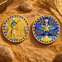 Two round Egyptian-themed coins displayed on sandy ground with rocks and a small decorative box nearby. One piece shows a gold-toned figure with blue and red accents, and the other shows a blue and gold winged figure with hieroglyphic details.