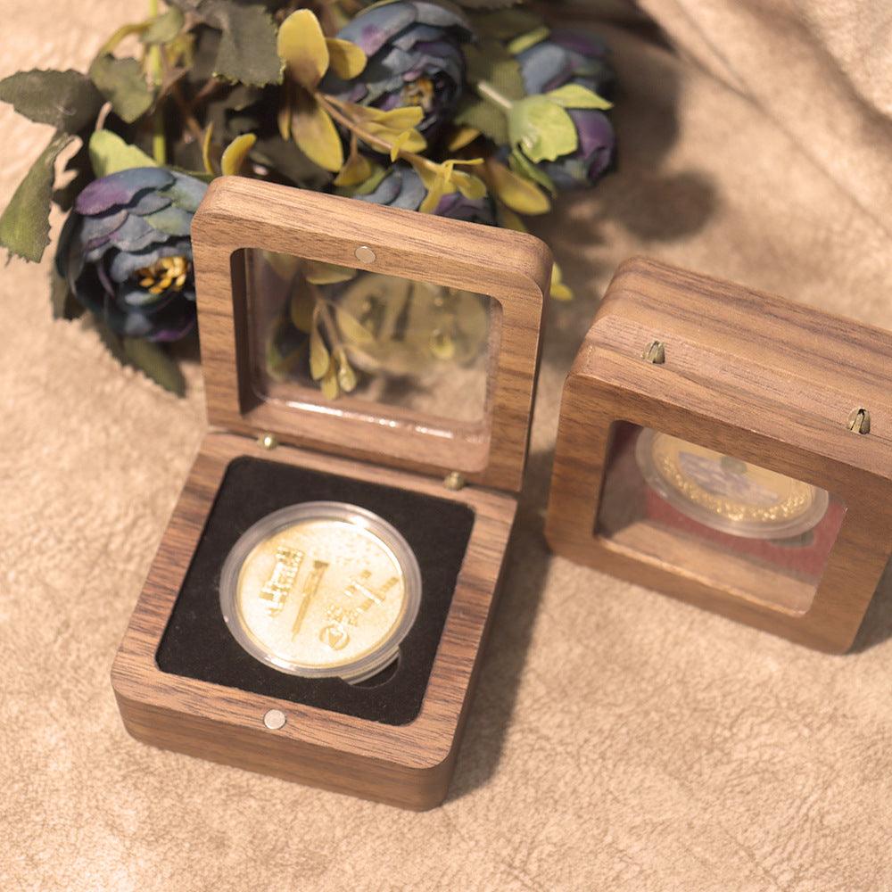 Gold coin in a wooden display case on a textured surface with flowers in the background